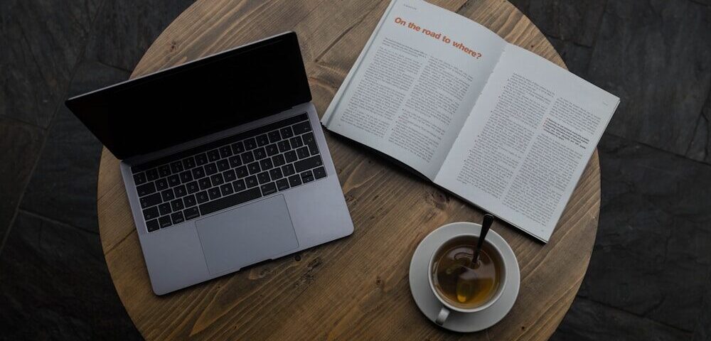 gray laptop beside white teacup and book
